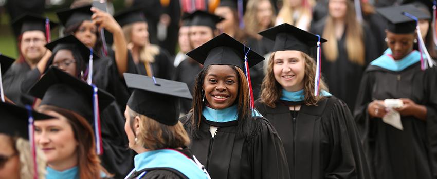 非裔美国女毕业生面带微笑，头戴礼帽，身穿长袍，排队走向毕业典礼.
