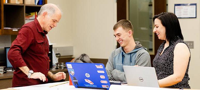 Student smiling looking at laptop with professors looking on.