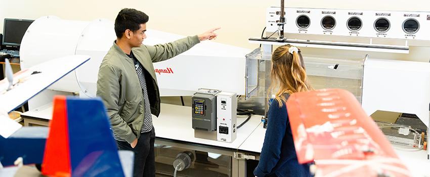 在机械实验室里，男学生指着一台机器.